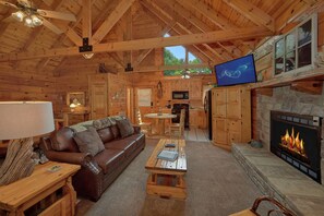 A cozy cabin interior with a wooden ceiling, a fireplace, a television, a sofa, and a dining table. - Value! | Games | Hot tub (Gatlinburg)
