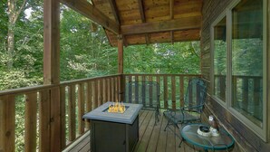 Una terraza de madera con una chimenea integrada, sillas de metal y una mesa de vidrio.