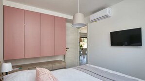 A bedroom with a bed, a large pink wardrobe, a television, and an air conditioning unit. - Irena Apartments (Konavle)