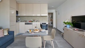 A modern kitchen with a dining area, a sofa, and a TV on a cabinet. - Irena Apartments (Konavle)