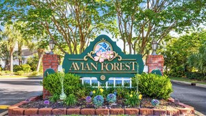 Un panneau indiquant l’entrée de la forêt d’Avian, avec une bordure en briques et un jardin aménagé.