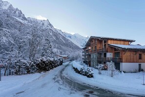 Une route de montagne enneigée menant à un chalet en bois doté de plusieurs balcons et d’une façade en pierre.