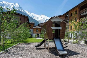 Un terrain de jeux avec un toboggan et une structure d’escalade, entouré de bâtiments et avec une montagne en toile de fond.