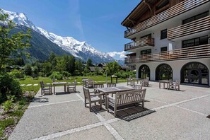 A hotel with outdoor seating, a mountain view, and a modern building with balconies.