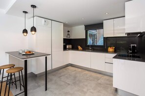 Una cocina moderna con una isla central, taburetes de bar y un ventanal con vistas a un edificio.