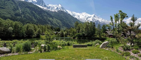 A mountain landscape with a lake, trees, and two lounge chairs facing the view.