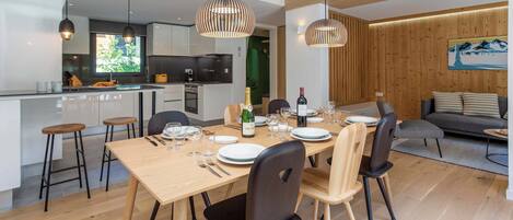 A modern kitchen with a dining area, wooden flooring, and pendant lighting.