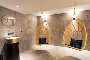Une salle de bain avec deux fauteuils suspendus en osier, un miroir rond et un lavabo moderne.