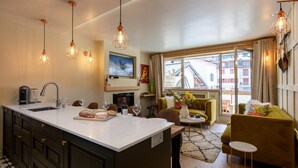 A modern kitchen with a large island, a dining area with a green sofa, and a living room with a fireplace.