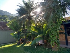 A garden with palm trees, a brick building, and a clear sky. - House for rent in Ubatuba on Lázaro Beach (Ubatuba)