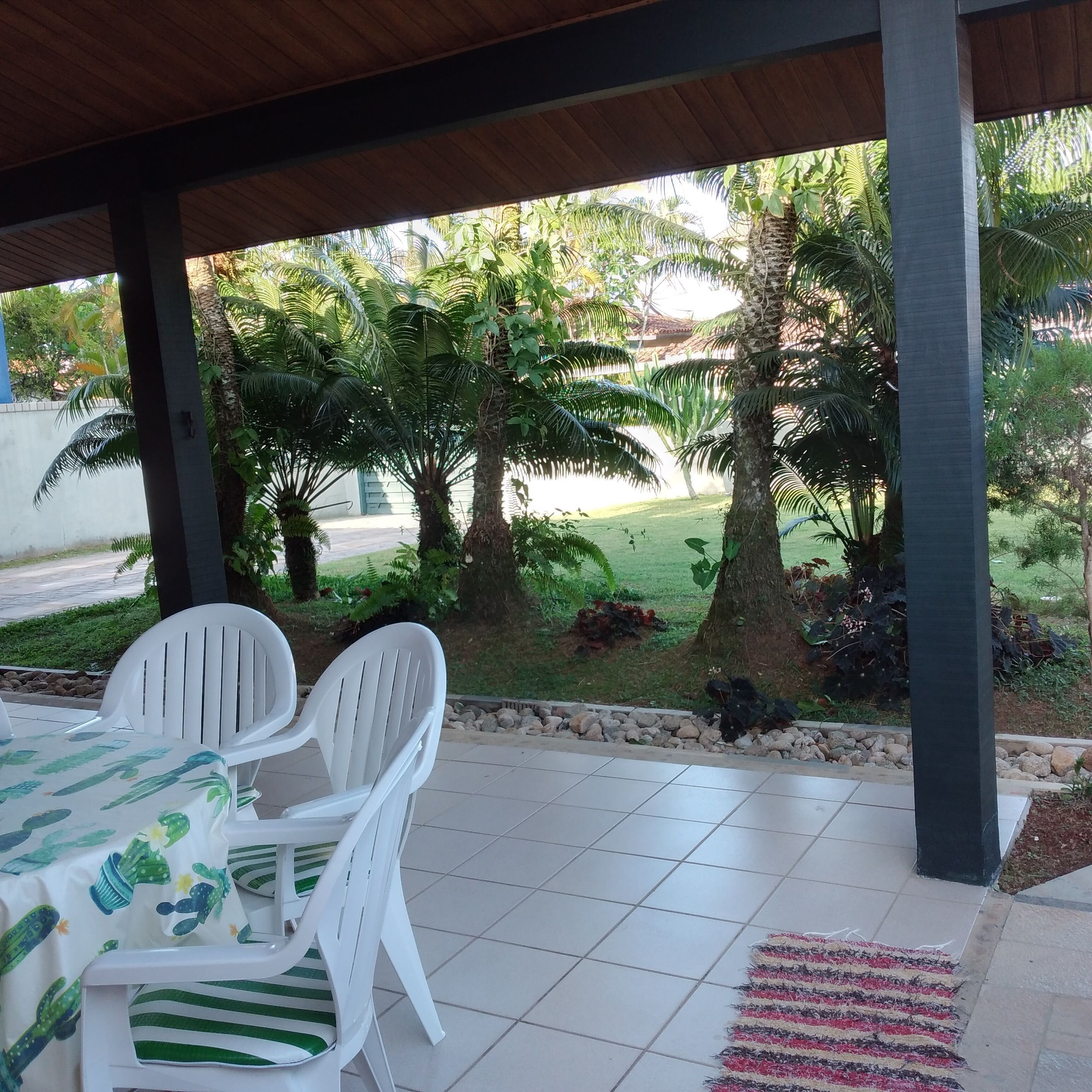 Eine Terrasse im Freien mit Tisch und Stühlen, umgeben von einem Garten mit verschiedenen Pflanzen und Bäumen.