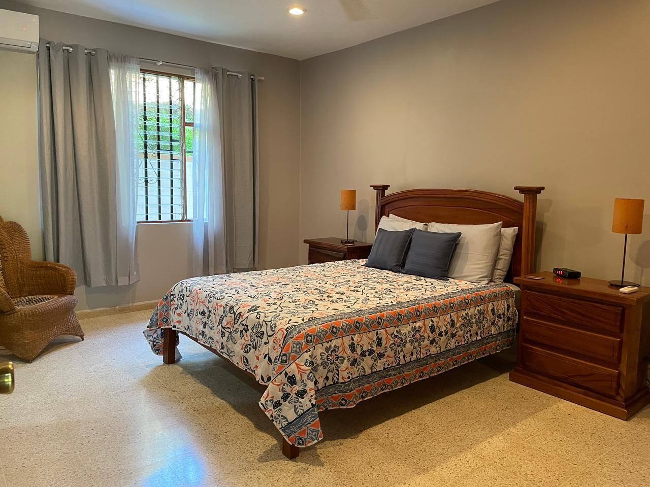 Une chambre à coucher avec un lit, des tables de chevet, une chaise et une fenêtre avec des rideaux.