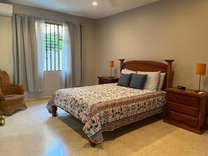 A bedroom with a bed, nightstands, a chair, and a window with curtains. - Cosy 2 bedroom and 2 bath condo walking distance to the beach. (Playas del Coco)