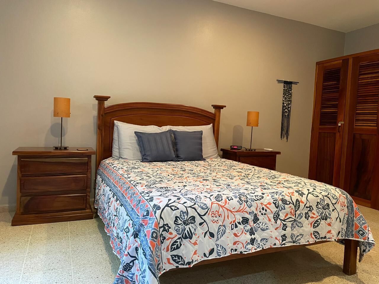 A bedroom with a bed, two nightstands, a wooden dresser, and a wardrobe.