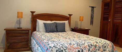 A bedroom with a bed, two nightstands, a wooden dresser, and a wardrobe.