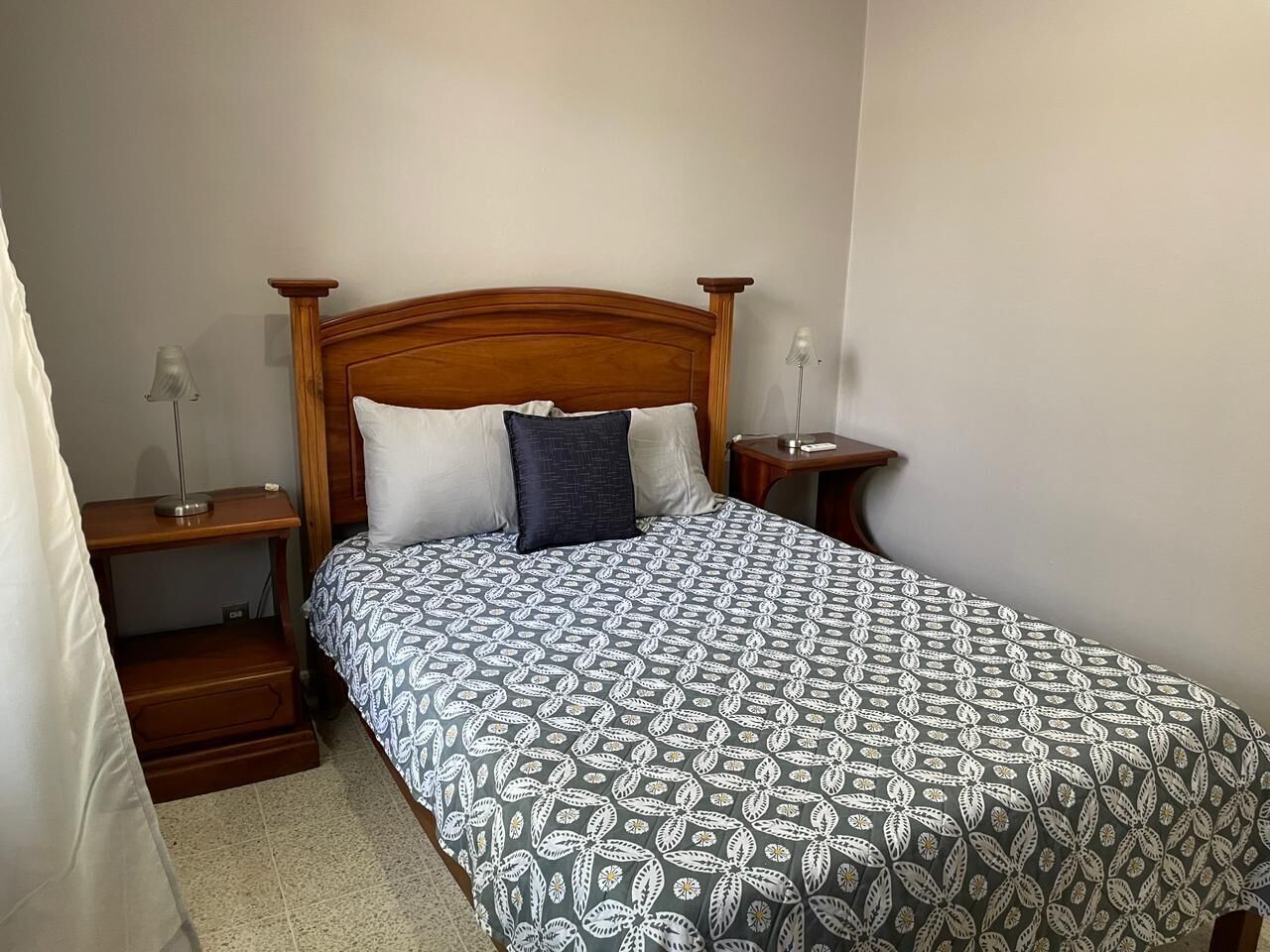 A neatly made bed with a patterned bedspread, wooden headboard, and two bedside tables with lamps.