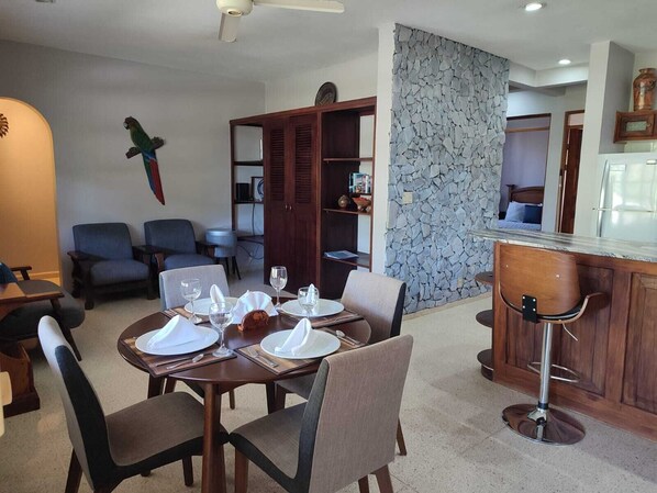 A dining area with a round table set for four, surrounded by chairs. There is a bar area with a high counter and stools. - Cosy 2 bedroom and 2 bath condo walking distance to the beach. (Playas del Coco)