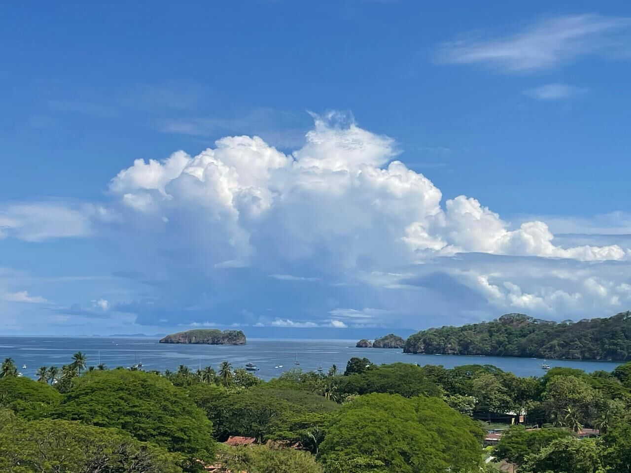 Un paisaje costero con vegetación exuberante, una gran formación de nubes e islas en la distancia.