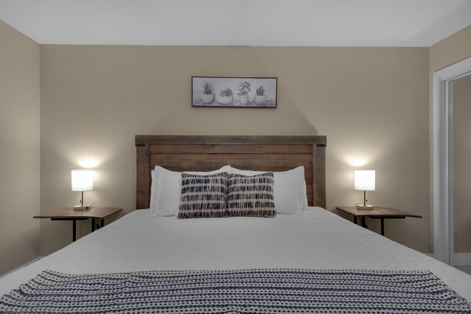 Quarto de hotel com uma cama grande, duas mesas de cabeceira com luminárias, uma cabeceira de madeira e um quadro na parede.
