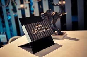 A black sign with 'ORTEGA HOTEL' in gold lettering on a stand, with a statue of a person in the background.