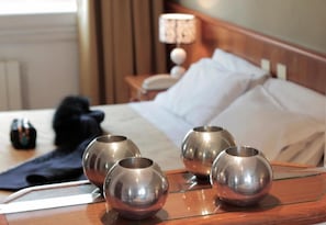 A hotel room with a neatly made bed, a bedside table with a lamp, and four metallic spherical objects on the table.