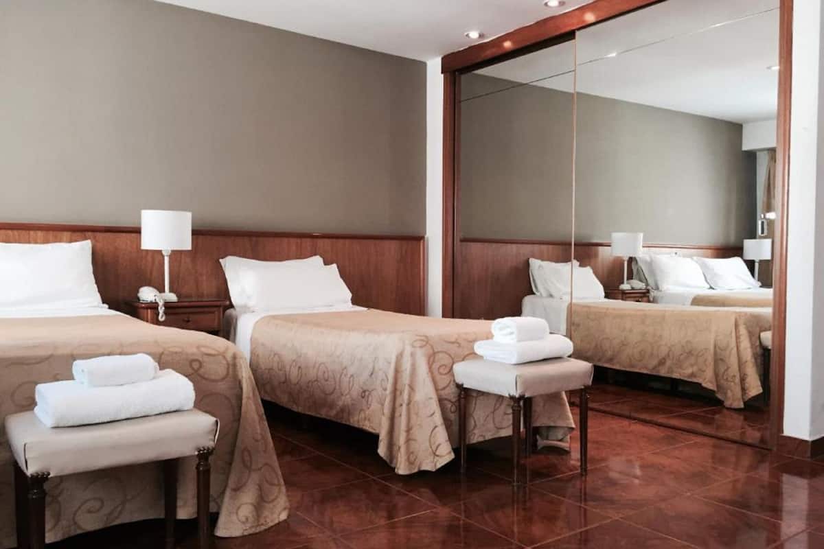 A hotel room with two beds, a large mirror, and a small table with a chair.