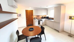 Une cuisine moderne avec des meubles blancs, une porte en bois, une table à manger avec des chaises et un lampadaire.