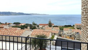 Une ville côtière aux bâtiments aux toits de tuiles rouges, offrant une vue dégagée sur la mer et sur des montagnes lointaines.