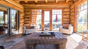 L’intérieur d’une cabane en rondins, avec un sol en pierre, des meubles en osier et une porte en verre donnant sur l’extérieur.