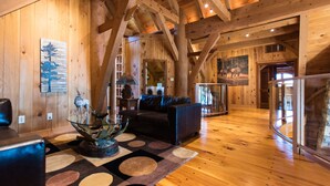 Un intérieur spacieux en bois, avec un plafond haut, une rambarde en verre et une cheminée.