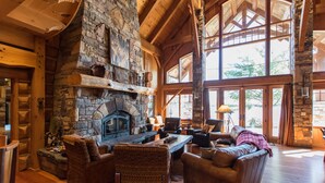L’intérieur d’une cabane en rondins, avec une cheminée en pierre, des poutres en bois et de grandes fenêtres.