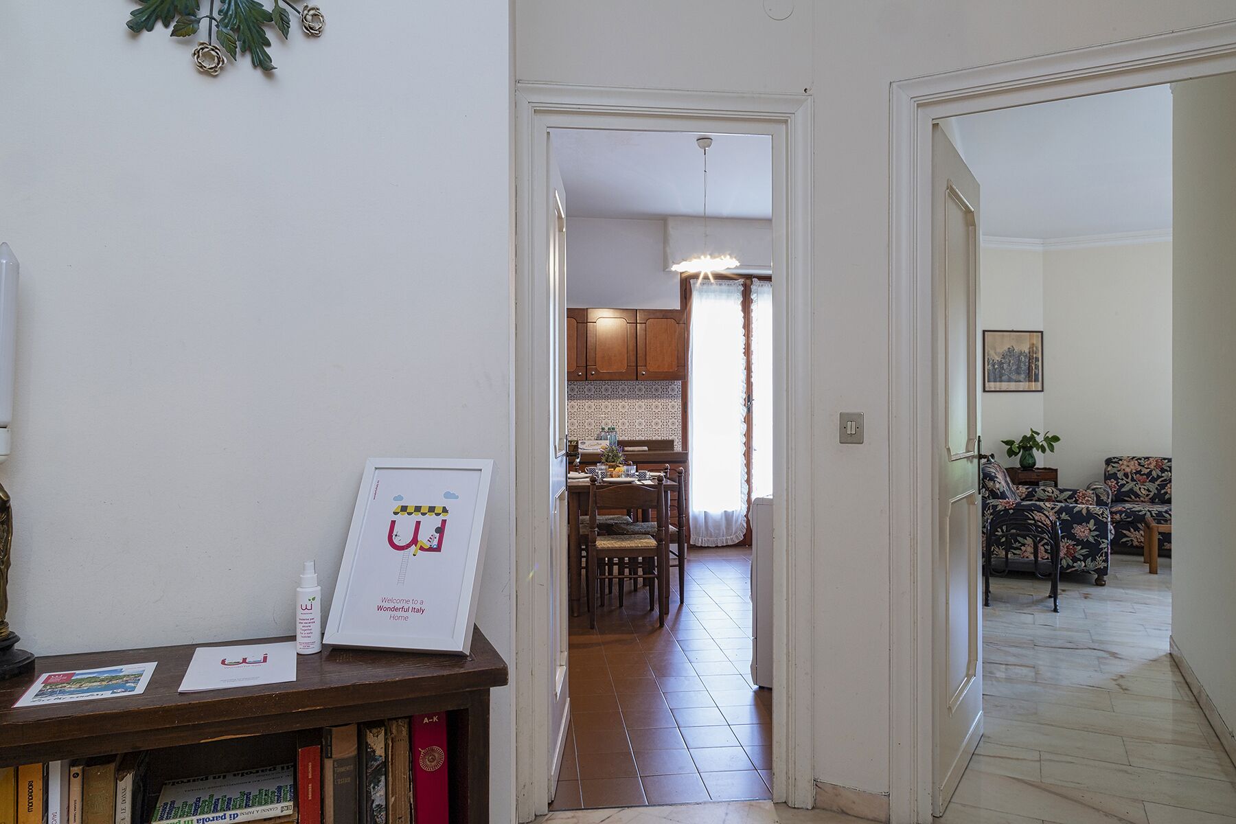 A hallway leading to a dining area with a table and chairs, a kitchen in the background, and a framed welcome sign on a shelf.