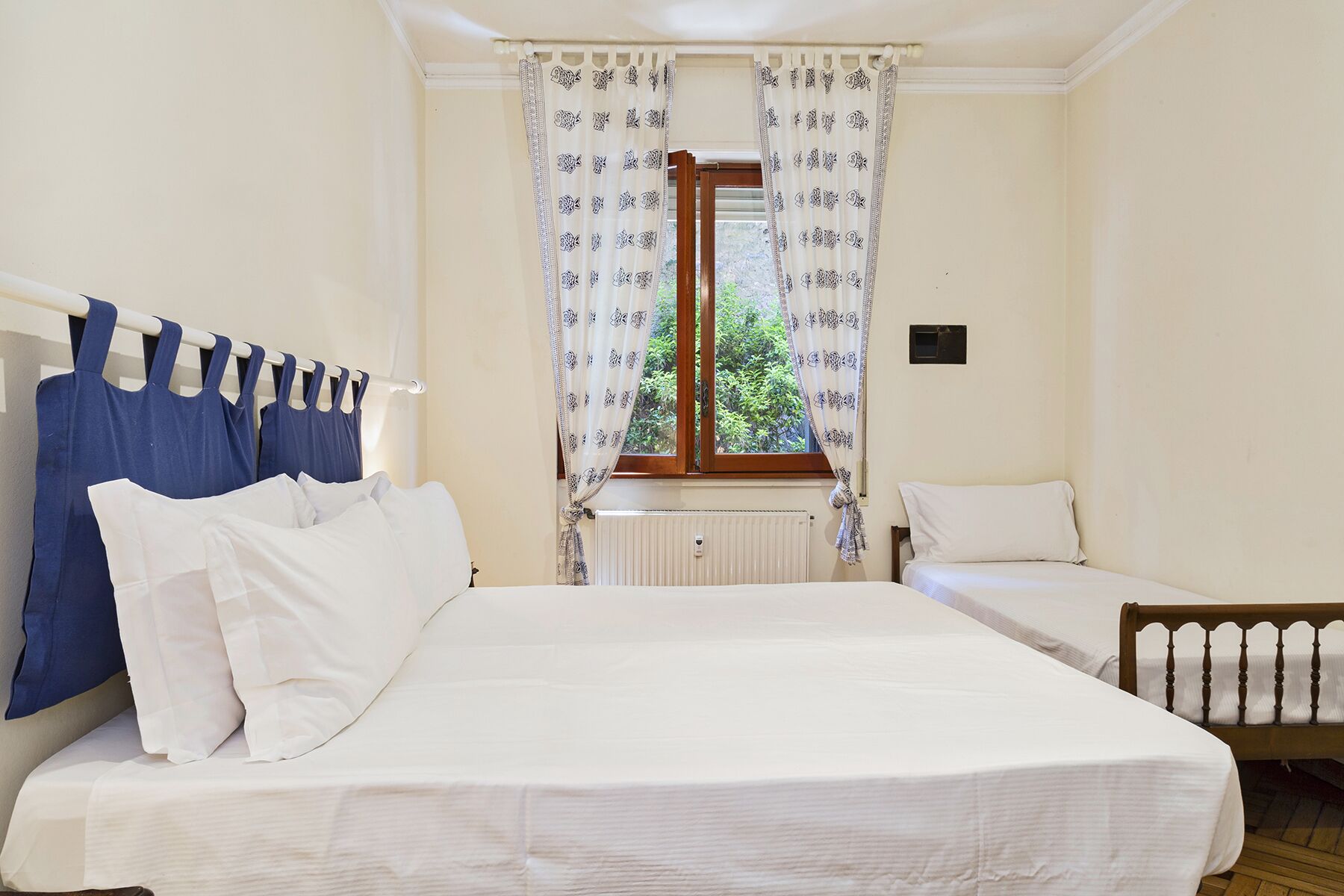 Une chambre avec deux lits, un radiateur et une fenêtre ornée de rideaux à motifs.