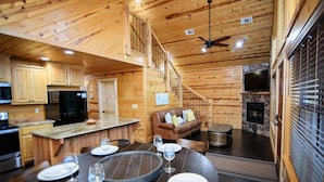 L’intérieur d’un chalet en bois comprend un coin repas, une cuisine, un salon et une cheminée.