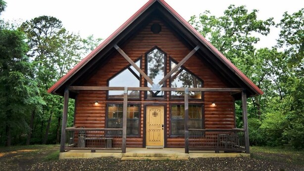 Une cabane en rondins avec une porte centrale, de grandes fenêtres et un porche doté de bancs.
