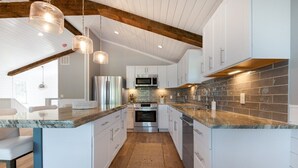 Una cocina moderna con armarios blancos, encimeras de granito y techo de madera.