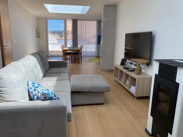 Un salon moderne avec un canapé, un pouf et un téléviseur à écran plat.