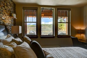 A hotel room with a large bed, a stone wall, and three windows offering a mountain view. - Cozens Pointe I-101 2 Bedroom Condo by RedAwning (Fraser)