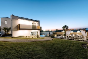 A modern two-story house with a swimming pool, outdoor seating, and a well-maintained lawn.