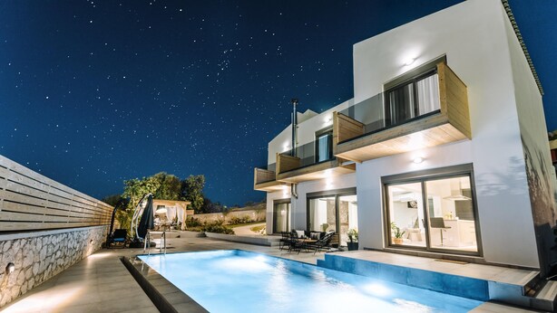 Una casa moderna con piscina, un muro de piedra y un cielo nocturno estrellado.