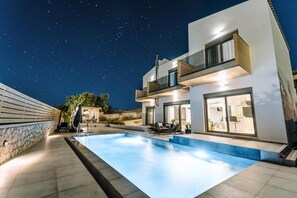 A modern house with a swimming pool, a stone wall, and a starry night sky.