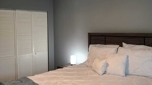 Een slaapkamer met een bed, nachtkastje, lamp en kledingkast.