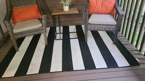 Een veranda met twee rieten stoelen, een bijzettafeltje en een gestreept vloerkleed.