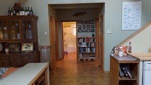 Een smalle gang met houten vloer, een houten kast aan de linkerkant, een boekenplank aan de rechterkant, en een tafeltje met flessen.