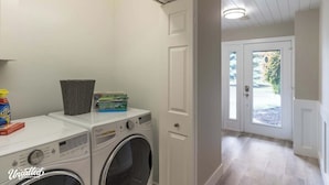 A laundry room with two washing machines, a basket, and detergent bottles.