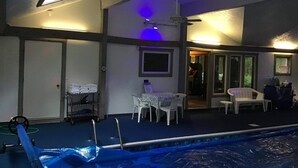 Una zona de piscina con un área cubierta, una mesa con sillas y un ventilador de techo.