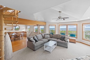 A spacious living area with a large gray sectional sofa, a white coffee table, and a wooden staircase.