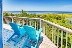 A wooden deck with two blue Adirondack chairs facing a scenic ocean view.
