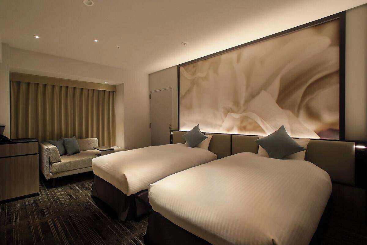 A hotel room with two beds, a sofa, a TV, and a large abstract wall art piece.