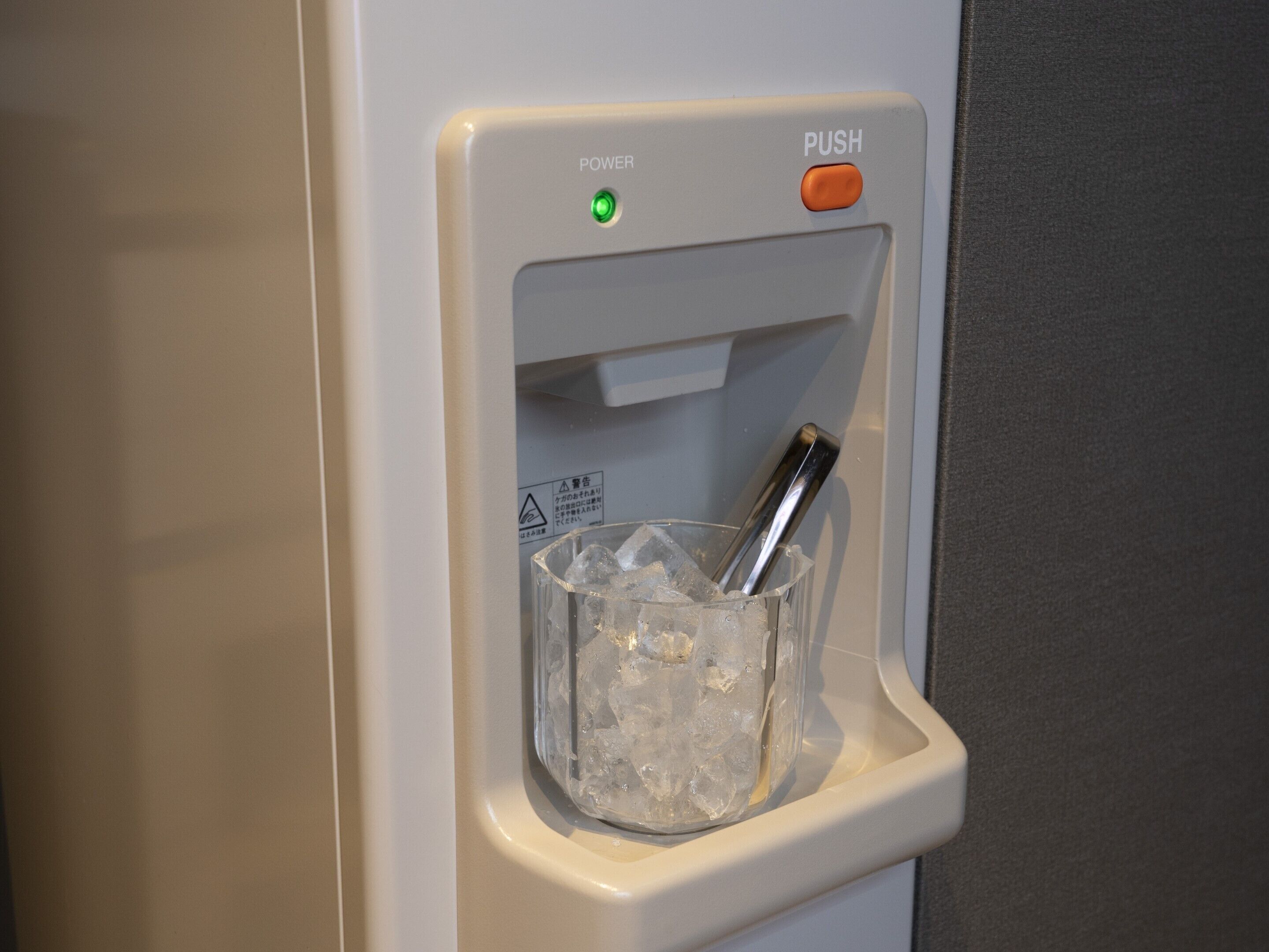 A water dispenser with a push button and a green indicator light, containing ice and a metal object.